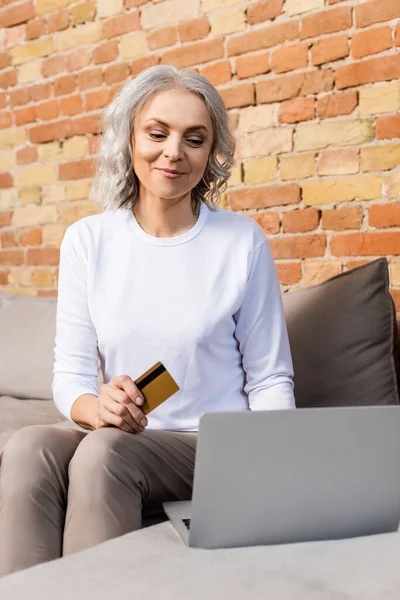 Selective focus of mature woman holding credit card near laptop — Stock Photo