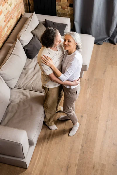 Над головой вид счастливой пары средних лет, держащейся за руки во время танцев дома — стоковое фото