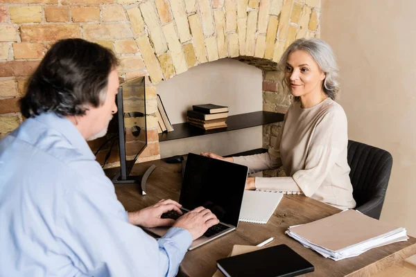 Selektiver Fokus der reifen Frau, wenn sie den Ehemann zu Hause auf der Laptop-Tastatur tippt — Stockfoto