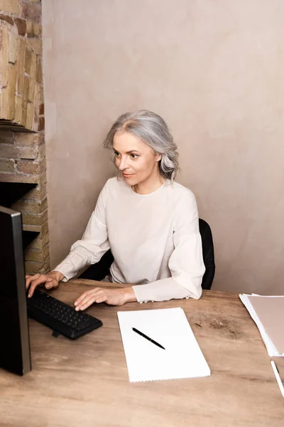 Mujer madura escribiendo en el teclado de la computadora en casa - foto de stock