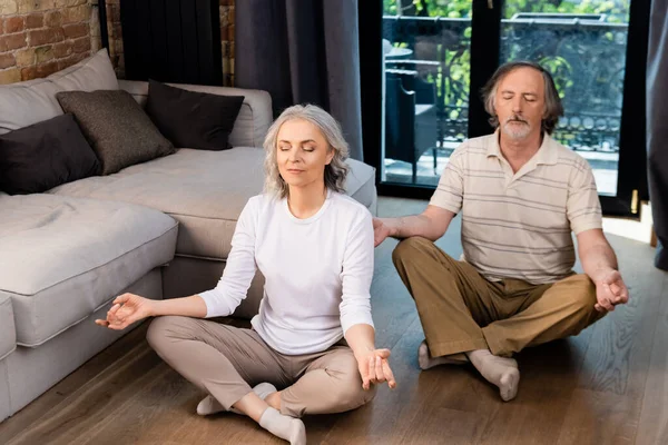 Relaxed mature couple with closed eyes sitting in lotus pose — Stock Photo