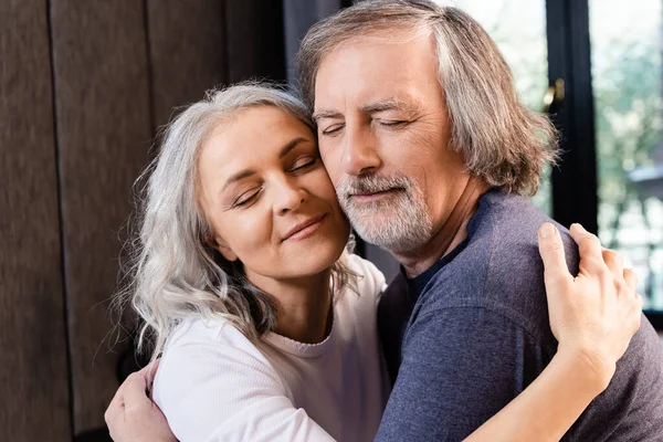 Happy middle aged couple with closed eyes hugging at home — Stock Photo