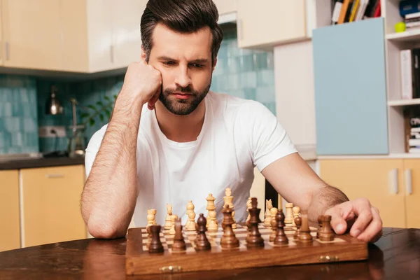 Selektiver Fokus eines nachdenklichen Mannes, der neben Schach auf einem Schachbrett am Tisch sitzt — Stockfoto