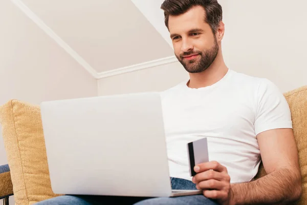 Enfoque selectivo del hombre usando el ordenador portátil y la celebración de la tarjeta de crédito en casa - foto de stock