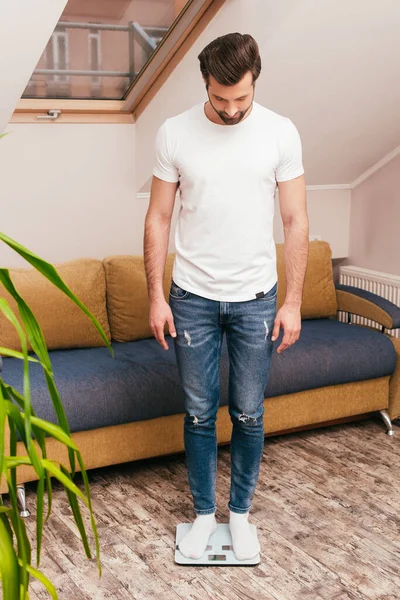 Bonito homem de pé em balanças na sala de estar — Fotografia de Stock