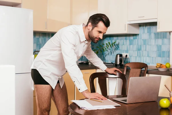 Vista lateral do homem de camisa e calcinha olhando para laptop perto de frutas na mesa — Fotografia de Stock