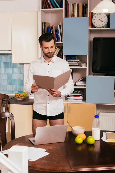 Focus selettivo di bell'uomo in camicia e mutandine che lavora con carte vicino al computer portatile e la colazione sul tavolo — Foto stock