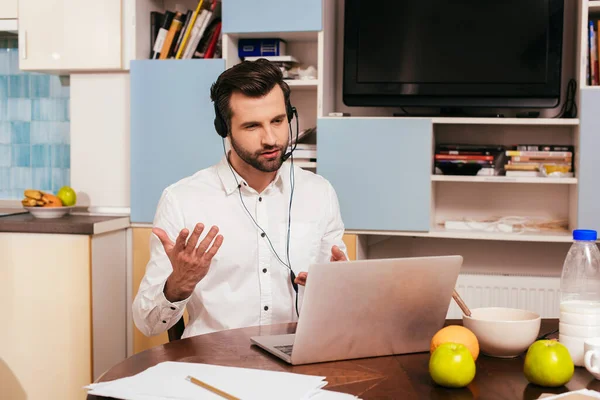 Handsome man using headset and laptop near breakfast in kitchen — Stock Photo