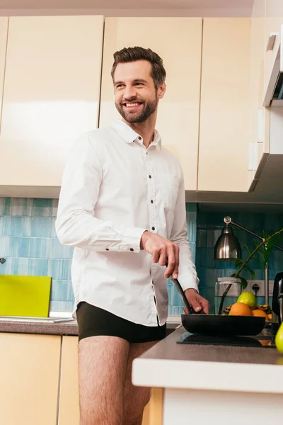 Focus sélectif de l'homme souriant en chemise et culotte cuisine petit déjeuner dans la cuisine — Photo de stock
