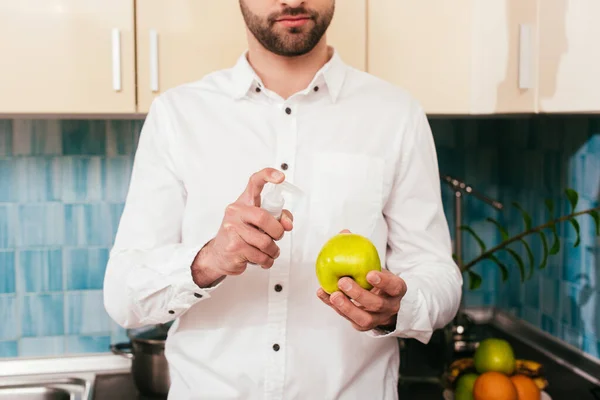 Vue recadrée de l'homme tenant désinfectant pour les mains et pomme dans la cuisine — Photo de stock