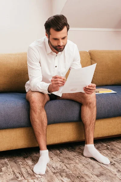 Schöne Freiberuflerin in Hemd und Höschen, die mit Papieren auf der Couch arbeitet — Stockfoto