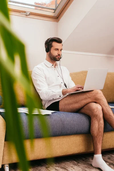 Selective focus of freelancer in shirt and panties using headset and laptop in living room — Stock Photo