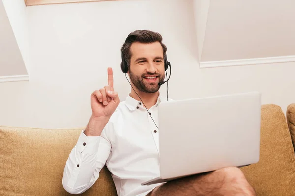 Selective focus of smiling freelancer in headset having idea during video call on laptop at home — Stock Photo