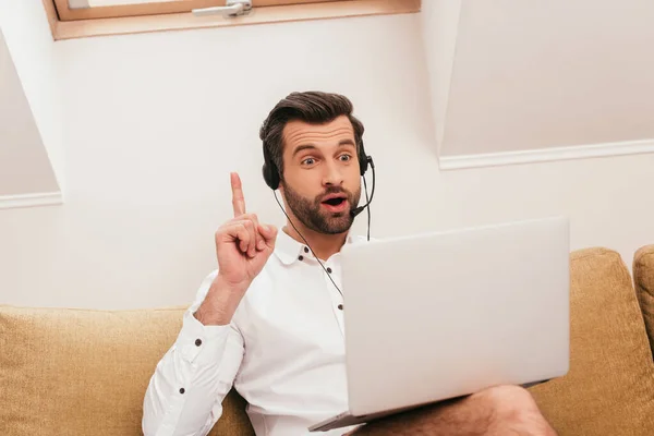 Selective focus of excited freelancer in headset having idea during video chat on laptop at home — Stock Photo