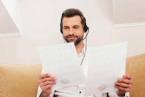 Selective focus of smiling teleworker in headset working with papers at home — Stock Photo