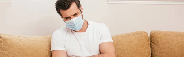 Colpo panoramico di uomo malato in maschera medica seduto sul divano a casa — Foto stock