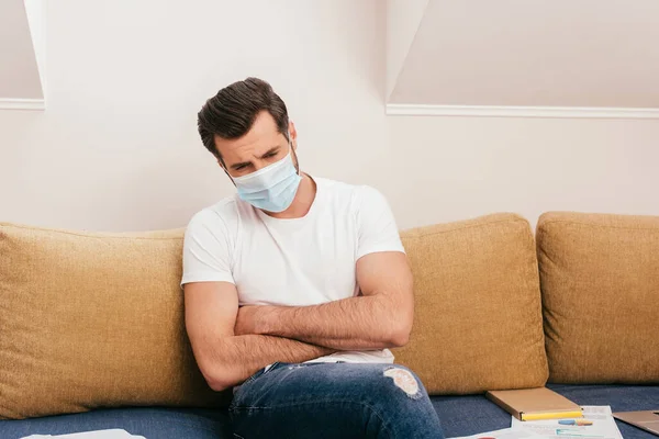 Kranker Freiberufler in medizinischer Maske sitzt neben Papieren auf Couch — Stockfoto