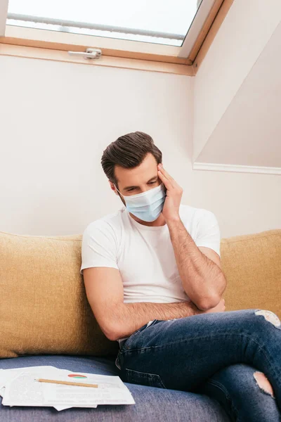 Selective focus of diseased freelancer in medical mask touching head on couch — Stock Photo