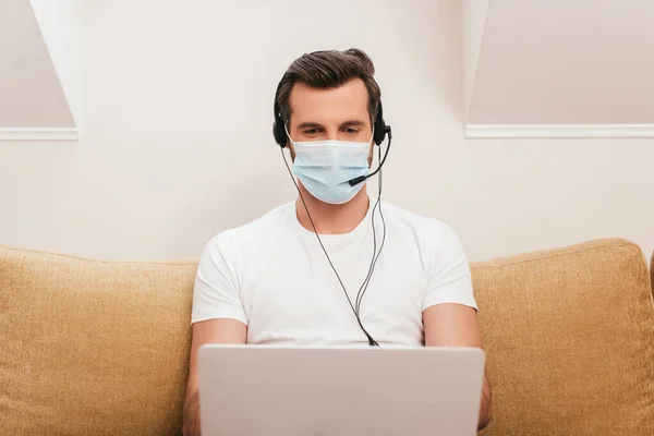 Focus selettivo del telelavoro in maschera medica utilizzando laptop e auricolare in soggiorno — Foto stock