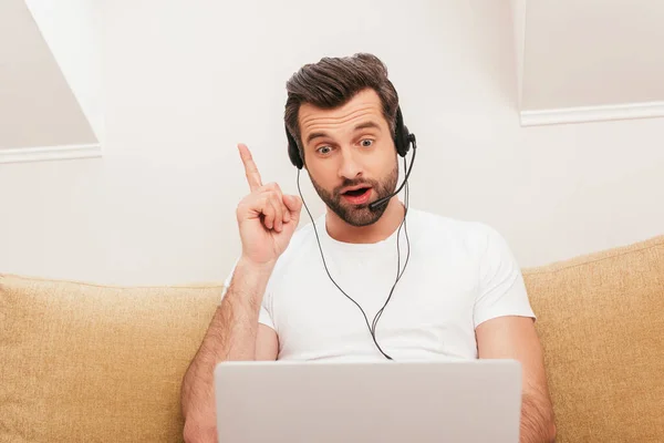 Surprised teleworker in headset having idea during video chat on laptop at home — Stock Photo