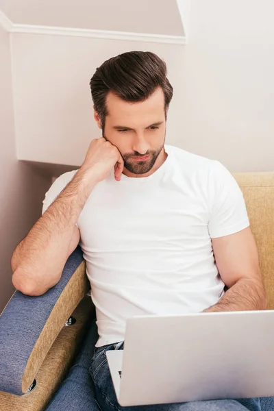 Teletrabajo guapo usando el ordenador portátil en el sofá en casa - foto de stock