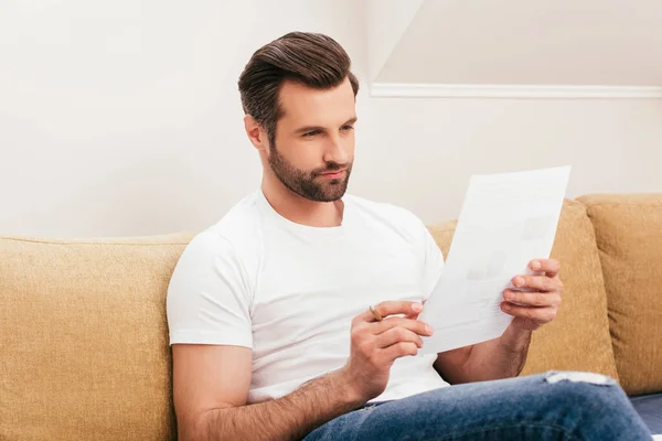 Selective focus of handsome freelancer holding pencil and document at home — Stock Photo