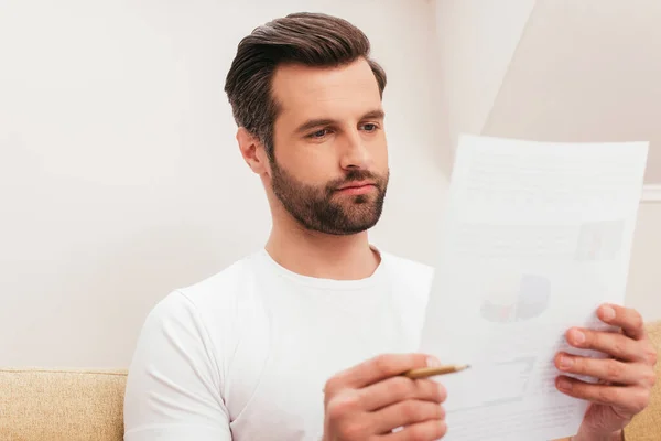 Selective focus of teleworker holding pencil and looking at document at home — Stock Photo