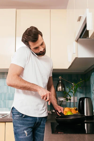 Hombre hablando en smartphone y preparando el desayuno en la cocina - foto de stock