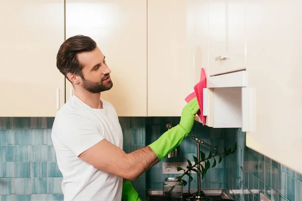 Vista laterale del bellissimo uomo che pulisce armadio in cucina — Foto stock