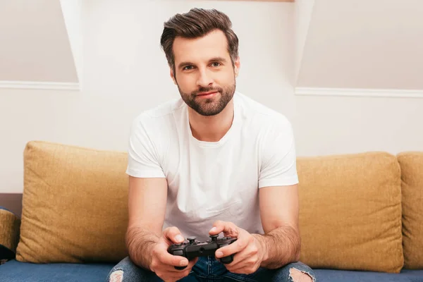 KYIV, UKRAINE - APRIL 14, 2020: Handsome man playing video game on couch — Stock Photo