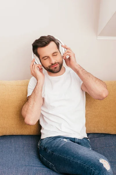 Красивий чоловік слухає музику в навушниках на дивані вдома — стокове фото