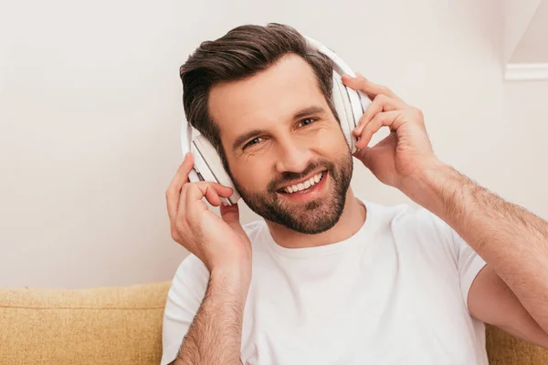 Handsome man in headphones smiling at camera on couch — Stock Photo