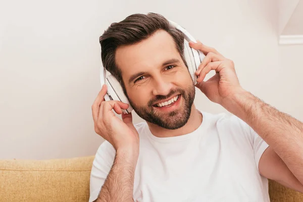 Beau homme dans un casque souriant à la caméra sur le canapé — Photo de stock