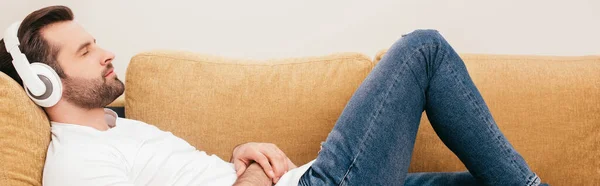 Side view of man in headphones listening music on couch, panoramic crop — Stock Photo