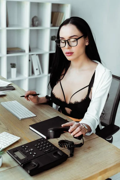 Seductive secretary in bra using telephone at table in office — Stock Photo