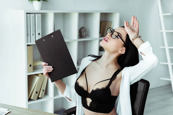 Verführerische Sekretärin mit Hand am Kopf, die Klemmbrett im Büro hält — Stockfoto