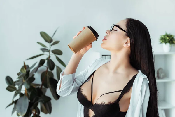 Sexy secretaria en anteojos y sujetador sosteniendo café para ir en la oficina - foto de stock