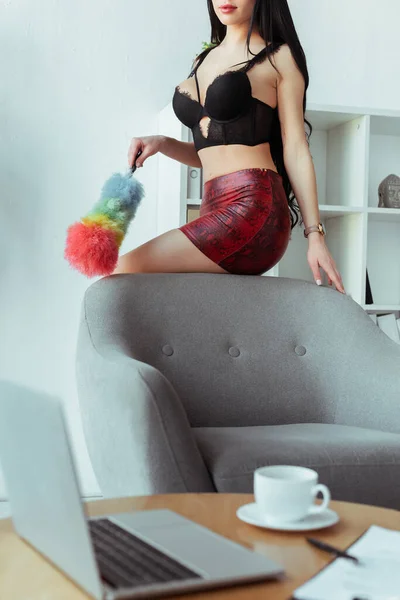 Selective focus of secretary in bra and skirt holding dust brush near armchair in office — Stock Photo