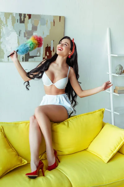 Fröhliches sinnliches Mädchen mit Staubbürste auf der Couch — Stockfoto