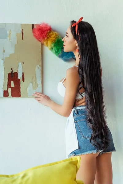 Vista posteriore della donna sensuale in reggiseno e grembiule pulizia pittura con pennello polvere — Foto stock