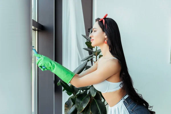 Side view of sensual woman in rubber gloves cleaning window at home — Stock Photo