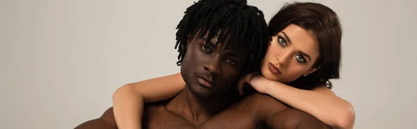 Sensual interracial pareja abrazo aislado en gris, concepto panorámico - foto de stock