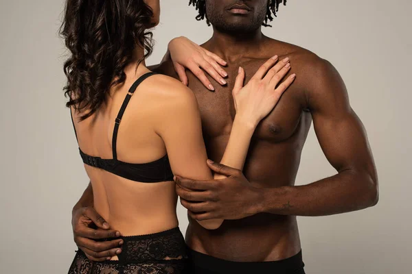 Partial view of multiethnic sexy couple hugging isolated on grey — Stock Photo