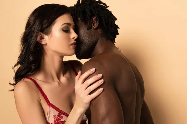 Shirtless african american man hugging and kissing attractive sexy woman on beige — Stock Photo