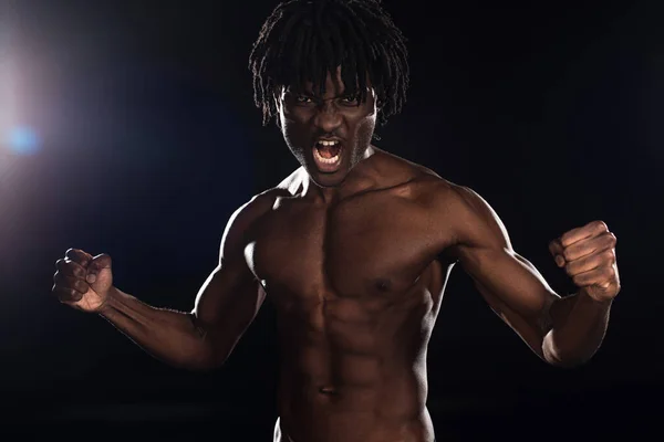 Muscular emocional afroamericano hombre gritando en negro con luz de fondo - foto de stock