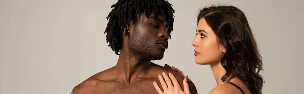 Pareja interracial íntima abrazándose y mirándose aislados en gris, encabezado del sitio web - foto de stock