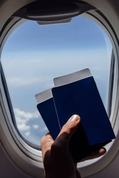 Cropped view of man holding in hand passports with air tickets near airplane porthole — Stock Photo