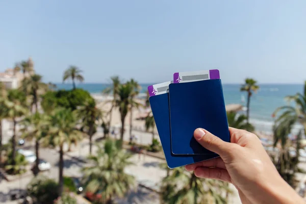Cropped view of man holding passports and air tickets with palm trees and sea coast at background — Stock Photo