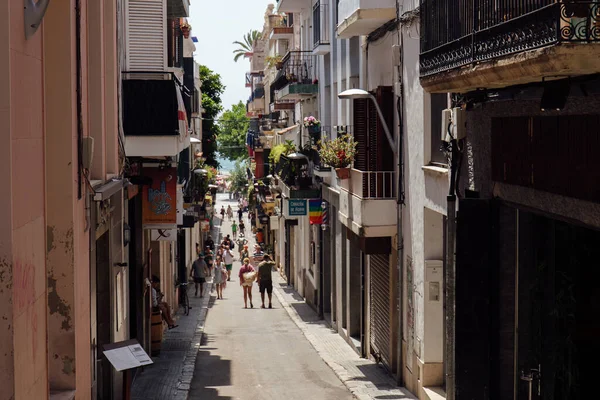 CATALONIA, ESPAÑA - 30 DE ABRIL DE 2020: Gente caminando por la calle urbana cerca de casas con plantas en el balcón - foto de stock