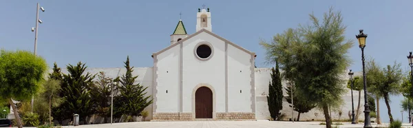 Recadrage horizontal d'arbres près de la façade blanche de la chapelle avec ciel bleu en arrière-plan en Catalogne, Espagne — Photo de stock